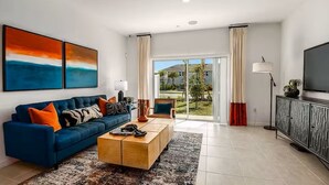 A modern living room with a blue sofa, a wooden coffee table, and a TV on a cabinet. - Furnished Model Home – Skye Ranch (Sarasota)