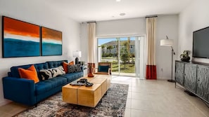 A modern living room with a blue sofa, a wooden coffee table, and a TV on a cabinet. - Furnished Model Home – Skye Ranch (Sarasota)
