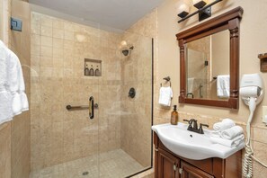 Un baño de hotel con ducha de vidrio, lavabo con tocador y espejo sobre el lavabo.
