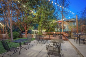 Un patio al aire libre con mesas y sillas, luces colgantes y una pérgola.