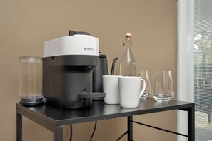 Eine Nespresso-Kaffeemaschine steht auf einem Tisch, zusammen mit zwei weißen Tassen, einem Glas und einer Flasche.