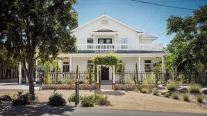 A two-story white house with a balcony, a stone wall, and a gravel driveway.