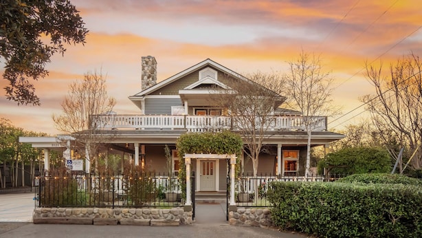 A two-story house with a porch, a stone chimney, and a gated entrance.