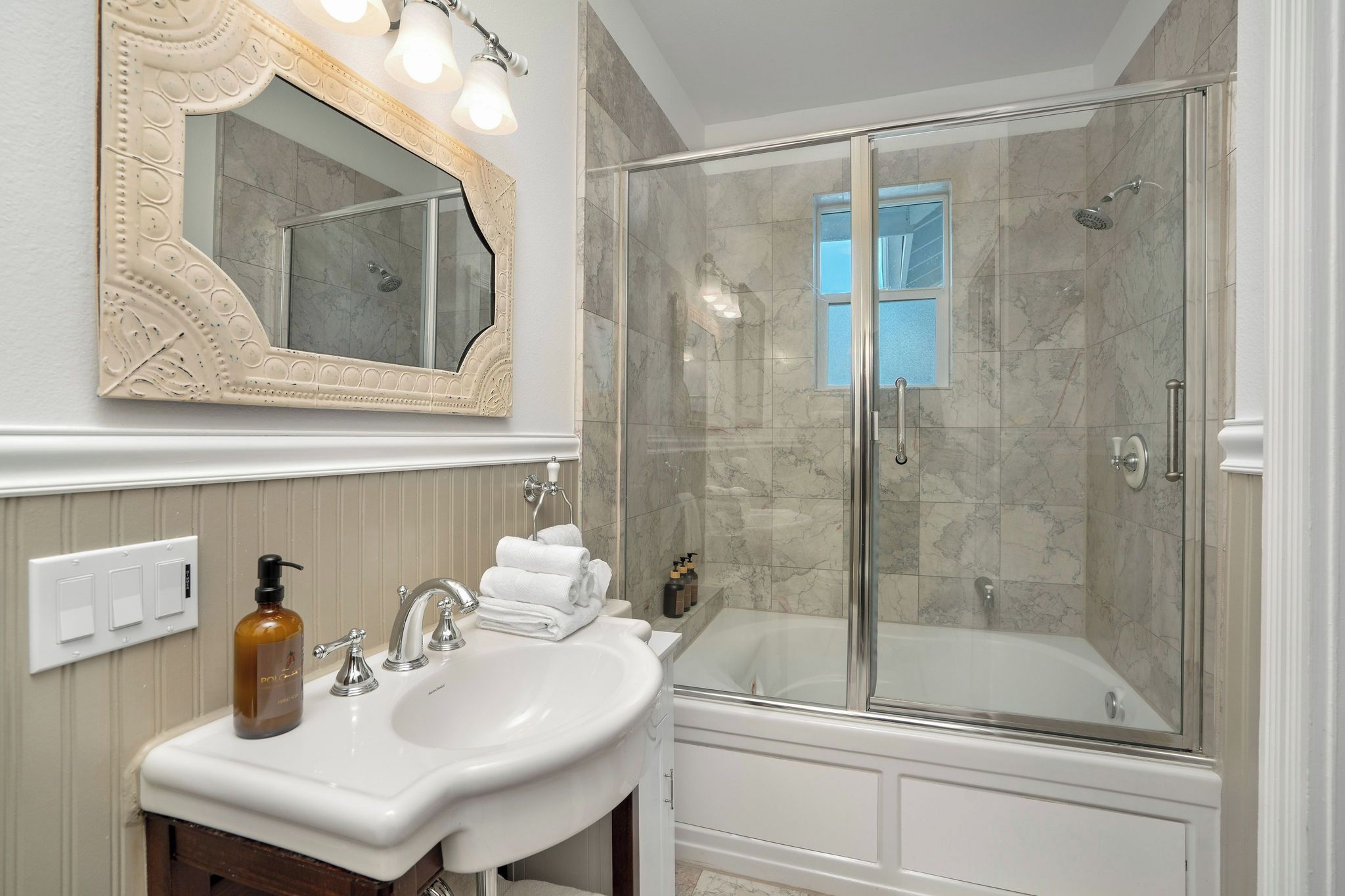 A bathroom with a large mirror, a sink, a glass-enclosed shower, and a bathtub.