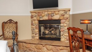A living room with a stone fireplace, a mounted television, a wooden chair, and a desk with a lamp.