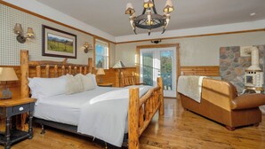 A bedroom with a wooden bed, a wooden bench, a chandelier, and a stone wall.
