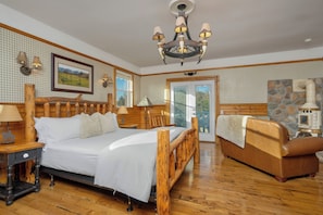 A bedroom with a wooden bed, a wooden bench, a chandelier, and a stone wall.