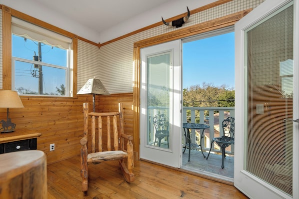 A wooden interior with a rocking chair, a table, and a balcony with chairs.