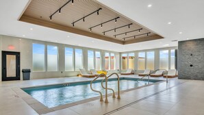 Indendørs swimmingpool med glasvægge, liggestole og et loft med trælameller og indbygningsbelysning.