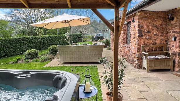 Un bain à remous, un espace salon extérieur, un mur en pierre et une pergola avec un plafond en bois.