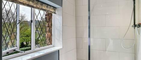 Un baño moderno con cabina de ducha de vidrio, una ventana con un adornado valance y vistas a la vegetación.