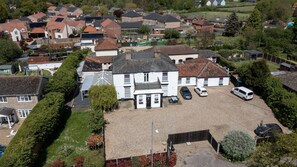 An aerial view of a residential area with houses, a large white building with a driveway, and parked cars. - Watton By Verve (Thetford)