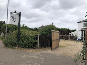 A gated entrance with a sign, a wooden fence, and a building with a white exterior. - Watton By Verve (Thetford)