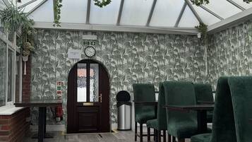 A greenhouse-style room with a wooden door, green chairs, and a clock on the wall.