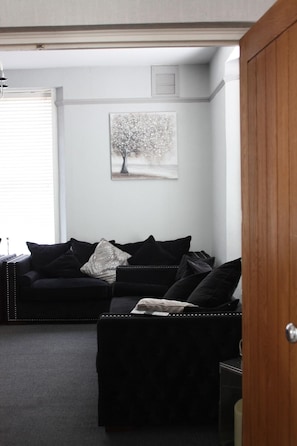 Una sala de estar con un sofá negro, un otomano negro más pequeño y un cuadro de un árbol en la pared.