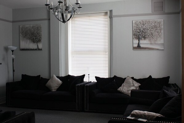 A living room with a black sofa set, a chandelier, and two wall-mounted paintings. - Watton By Verve (Thetford)