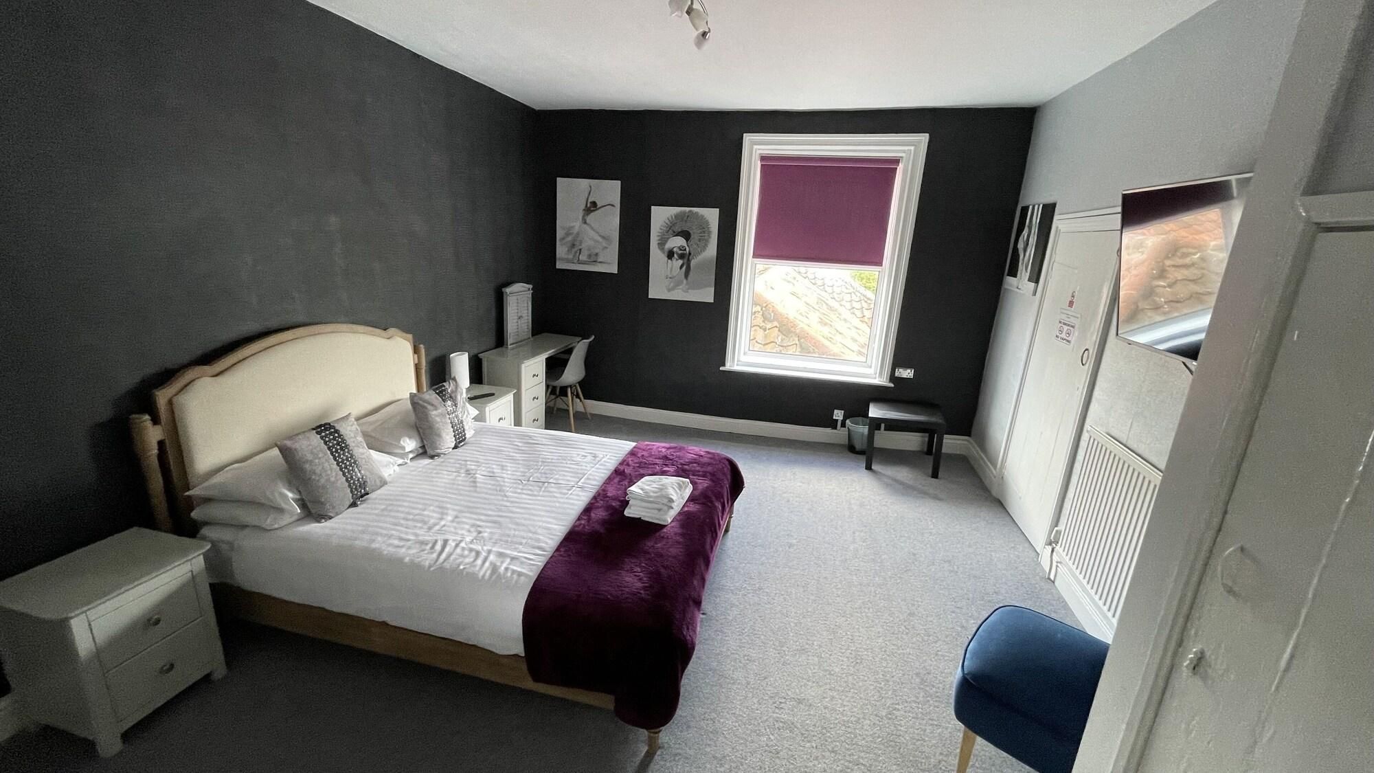 A bedroom with a bed, bedside tables, a desk, a chair, a window with a view, and artwork on the walls.