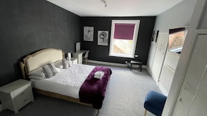 A bedroom with a bed, bedside tables, a desk, a chair, a window with a view, and artwork on the walls. - Watton By Verve (Thetford)