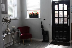 Una habitación con una silla roja, un escritorio con un globo terráqueo, una ventana con flores y una puerta negra.
