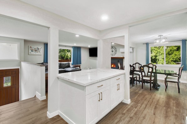 Una cocina moderna con armarios blancos, encimera de mármol y un comedor con sillas y mesa de madera.