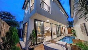 A modern two-story house with a glass-enclosed patio, a swimming pool, and outdoor furniture. - Kammara 1 Villa Bali (Canggu)