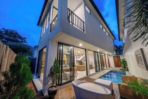 Ein modernes, zweistöckiges Haus mit einer verglasten Terrasse, einem Swimmingpool und Gartenmöbeln.
