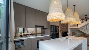 A modern kitchen with a large island, built-in appliances, and a stone accent wall. - Kammara 1 Villa Bali (Canggu)