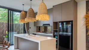 A modern kitchen with a central island, pendant lights, and a refrigerator. - Kammara 1 Villa Bali (Canggu)