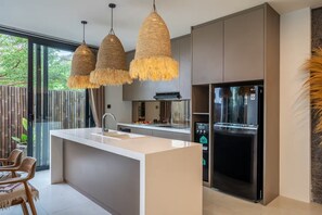 Eine moderne Küche mit Kochinsel, Pendelleuchten und einem Kühlschrank.