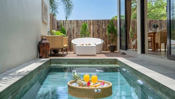 A swimming pool with a floating basket containing fruits and drinks, a hot tub, and a wooden fence in the background. - Kammara 1 Villa Bali (Canggu)