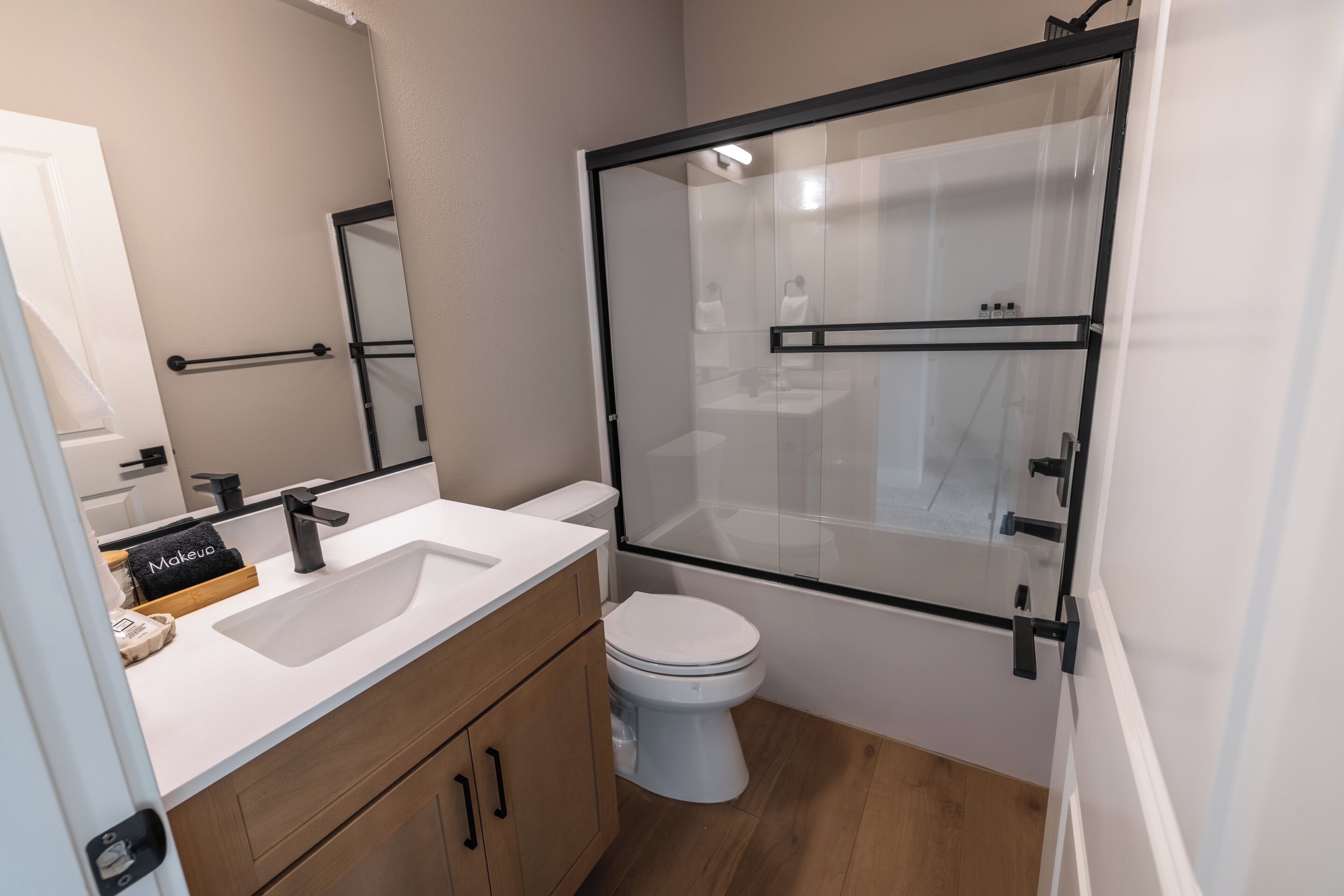 Een moderne badkamer met een wit wastafel, houten wastafelmeubel, een glazen douchecabine en een wit toilet.