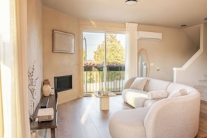 A modern living room with a sofa, a coffee table, a flat-screen TV, and a balcony with a view of trees and flowers. - “Cooper Mtn Retreat• Chef Kitchen • Mt. Hood View • Sleep 6 • Nike & Intel” (Beaverton)