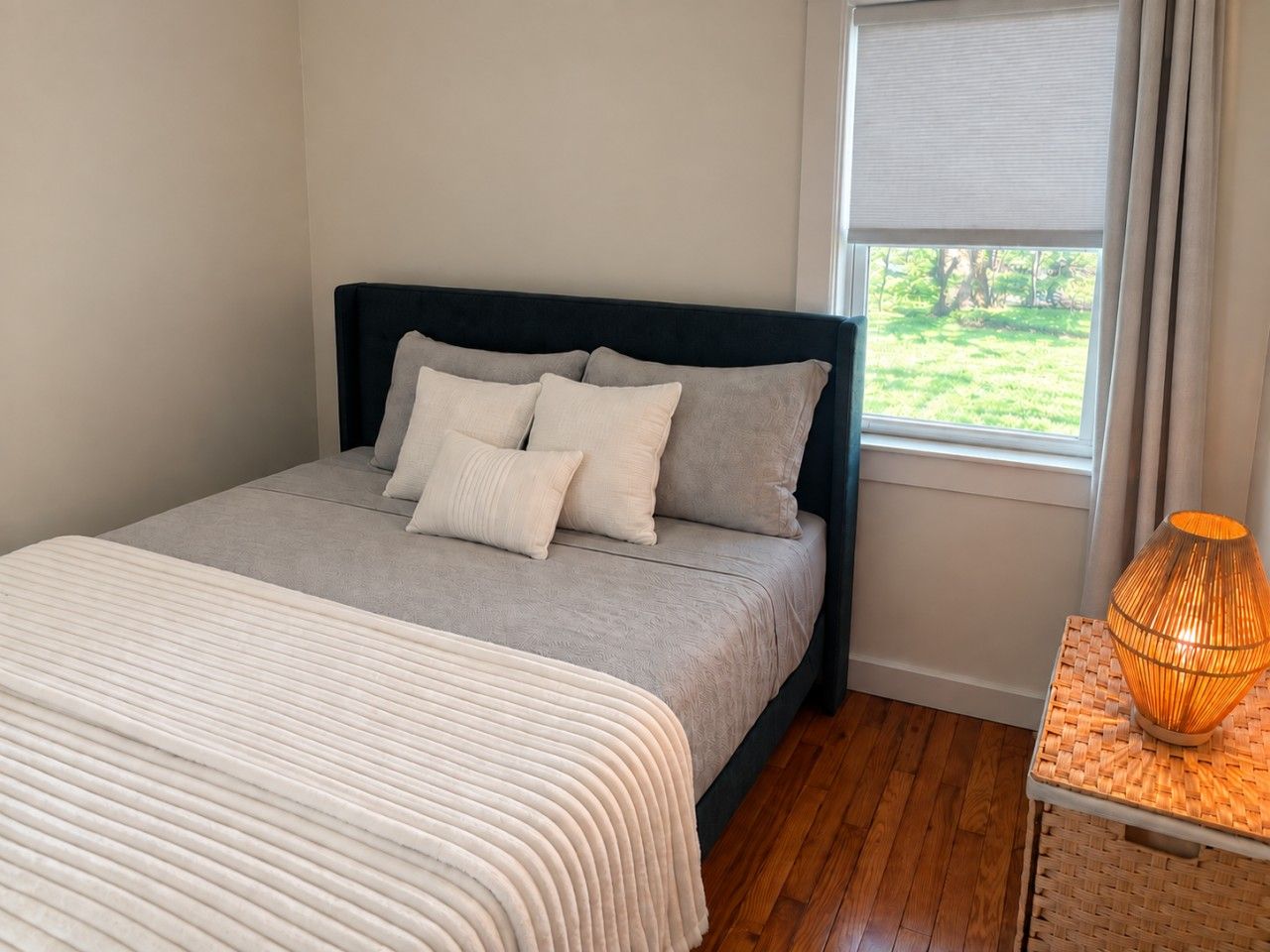 Un dormitorio con cama, almohadas, lámpara de noche y ventana con vistas.