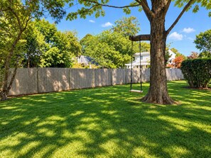 Ein Garten mit Schaukel, Holzzaun und Baum.