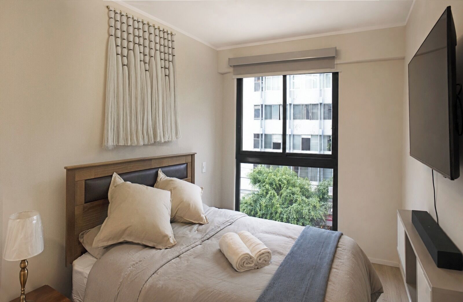 Un dormitorio con cama, ventana, televisor y una obra de arte colgada en la pared.
