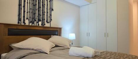 A hotel room with a bed, a headboard, a wall-mounted macrame decoration, a bedside lamp, and a wardrobe.
