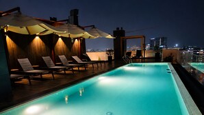 A rooftop swimming pool with lounge chairs and umbrellas, surrounded by city buildings.