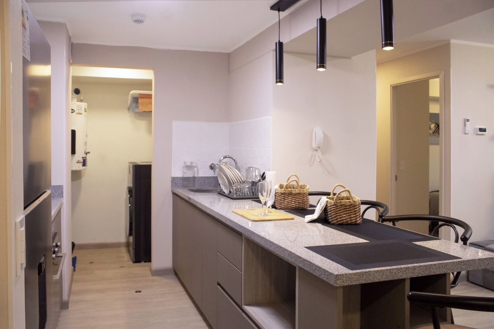 Una cocina moderna con una isla central, luces colgantes y una zona de comedor con una silla.