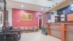 A reception area with a reception desk, a bench seating area, and a large framed artwork on the wall. - Formerly Reddoorz Syariah Plus @ Banjarbaru 2 (Banjarbaru)