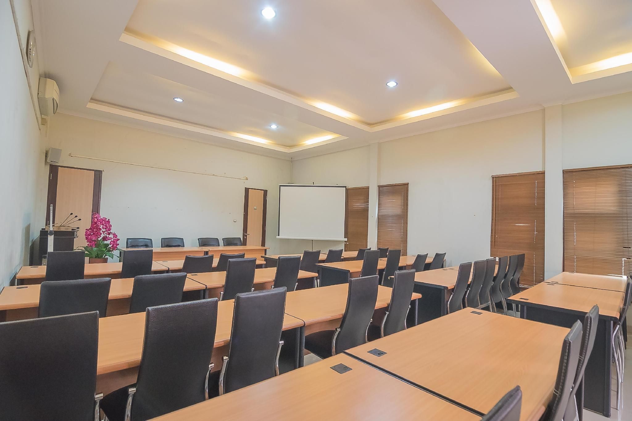 A conference room with multiple tables, chairs, a whiteboard, and a projector screen.