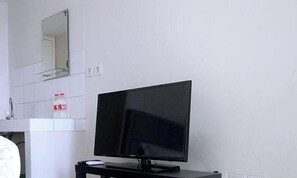 A room with a television on a stand, a mirror above the TV, and a bottle of water on the wall. - Springlake Apartment Summarecon by Veeroom by Zuzu (Bekasi)
