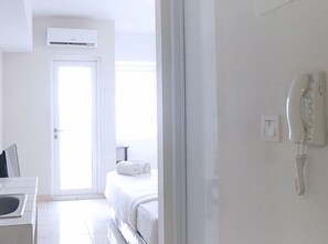 A hotel room with a bed, a bathroom, a sink, a telephone, and an air conditioning unit. - Springlake Apartment Summarecon by Veeroom by Zuzu (Bekasi)
