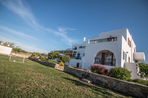 A white building with a stone retaining wall, a small garden, and a clear blue sky. - Lefteris Studios (Naxos)