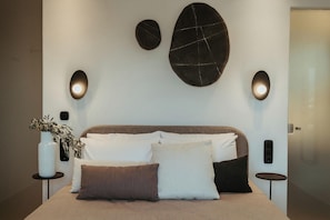 Un dormitorio moderno con una cama, dos mesitas de noche, una lámpara de pared y una planta en maceta.