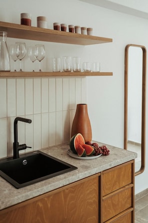 Una cocina con un lavabo negro, armarios de madera, encimera de mármol, un jarrón y un plato con fruta.