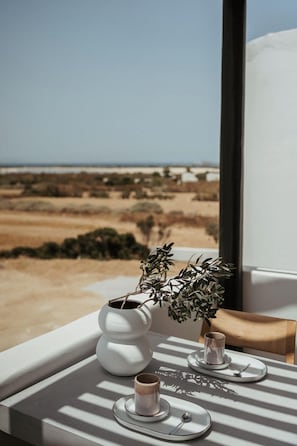Una mesa con una planta en maceta, dos tazas y platillos junto a una ventana con vistas a un paisaje desértico.