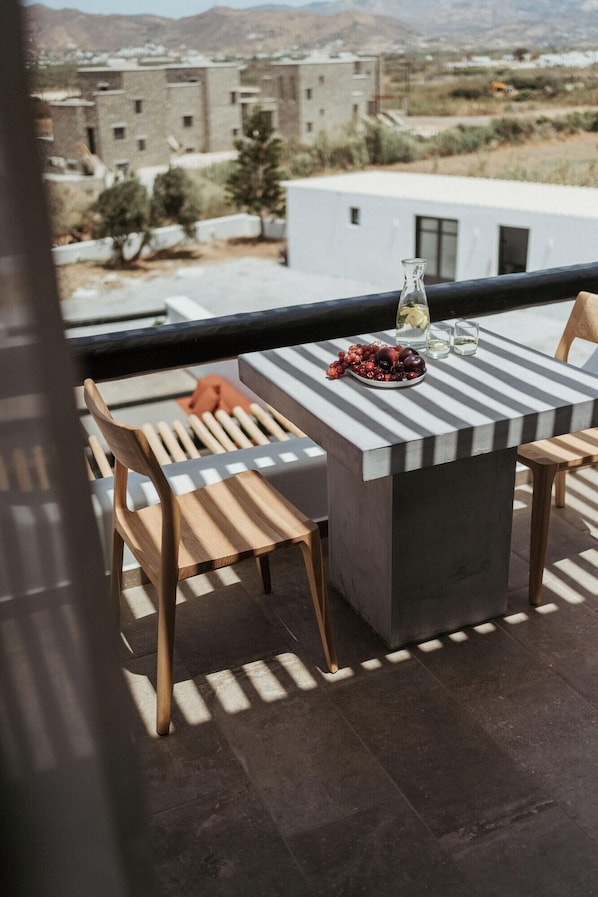 Un balcón con una mesa, sillas, una botella y un cuenco de fruta.