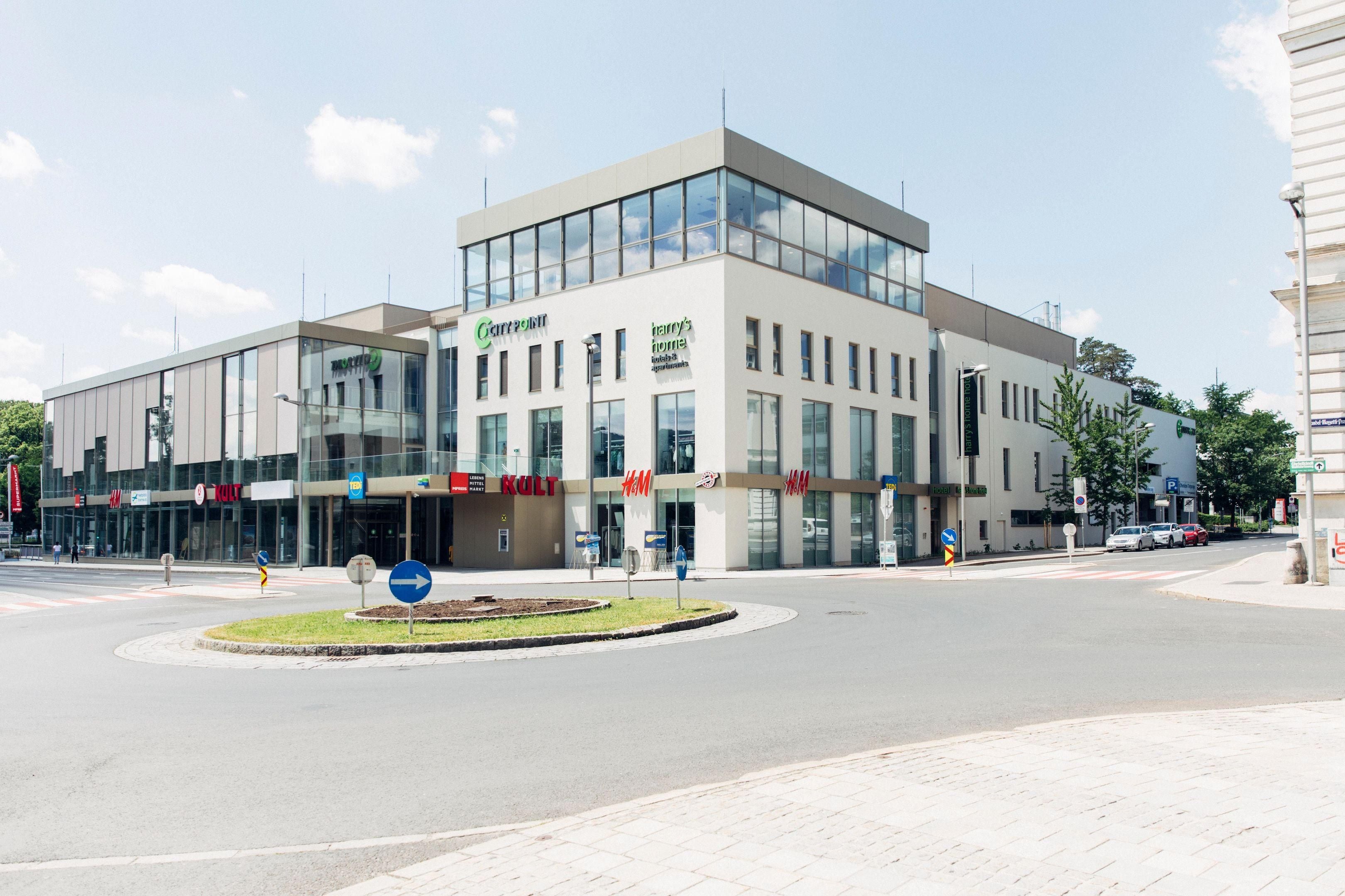 A modern building with large glass windows, a central entrance, and signage for 'Cartridge,' 'Harry's,' and 'KULT.'