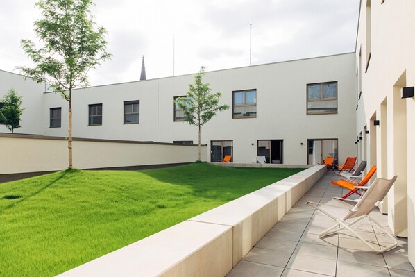 A courtyard with a green lawn, outdoor seating area, and a modern building facade.