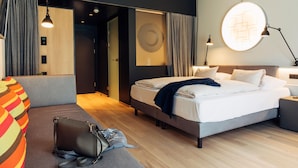 Una habitación de hotel moderna con cama, mesitas de noche, un escritorio, una silla, un sofá y una maleta.
